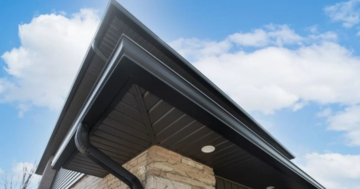 Close-up of black eavestroughs and soffits on a modern home with stone exterior under a blue sky